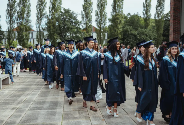 Constructor University graduates in blue caps and gowns walk together in an outdoor procession