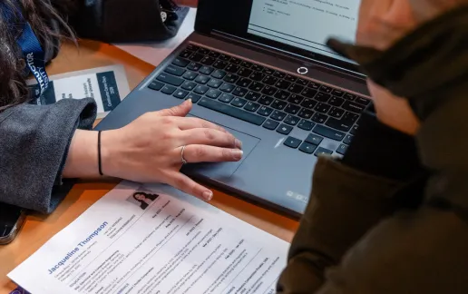 Two people review a CV on a laptop at a university career support table