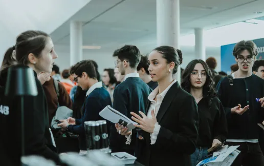 A student holding a notebook speaks with an at a busy university career fair