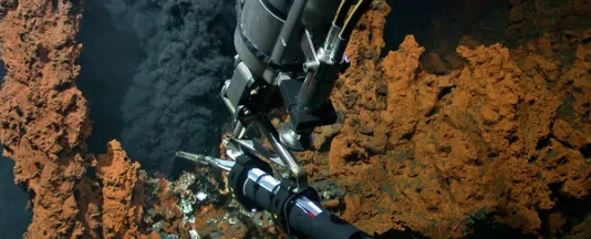 A hydrothermal vent on the Mid-Atlantic Ridge. Hot, mineral-rich fluids are distributed throughout the ocean via the dispersion cloud, known as the plume. The photo was taken during the M190 research expedition with the MARUM-QUEST4000 remotely operated vehicle. The arm of the robot holds a temperature lance into the plume to measure the temperature there. Photo: MARUM – Center for Marine Environmental Sciences, University of Bremen. 