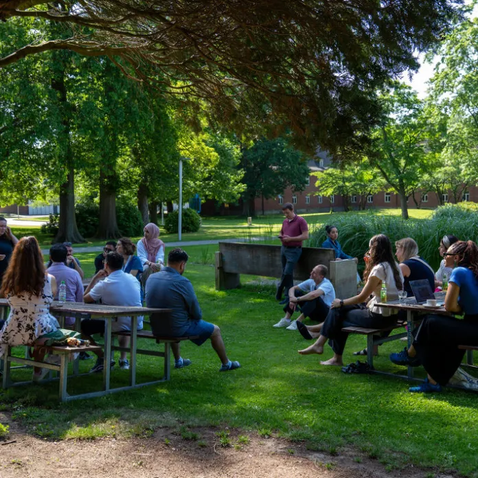 Participants sit at tables and talk during an outdoor event on a university campus