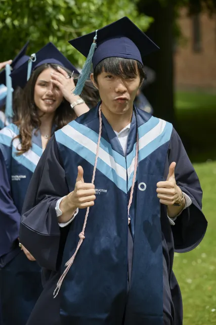 A smiling Constructor University graduate gives two thumbs up outdoors