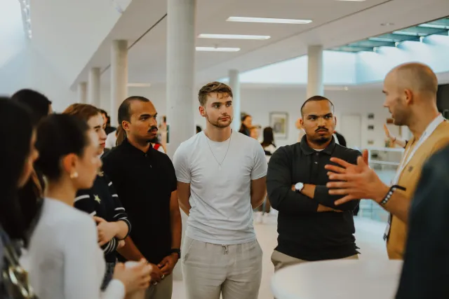 A group of event attendees listen to a presenter during a networking discussion on campus